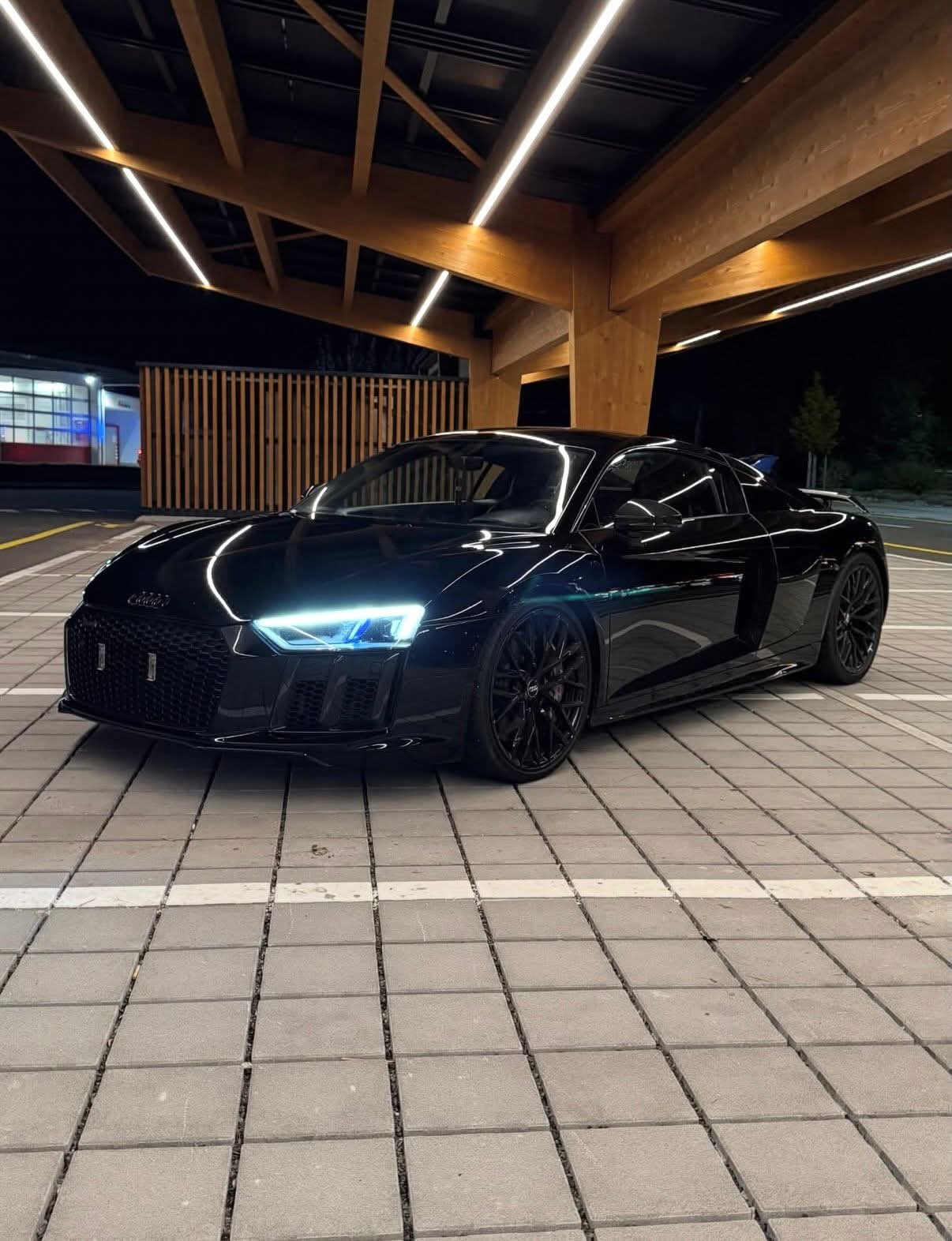 Audi R8 V10 noire, de nuit, sous un auvent en bois