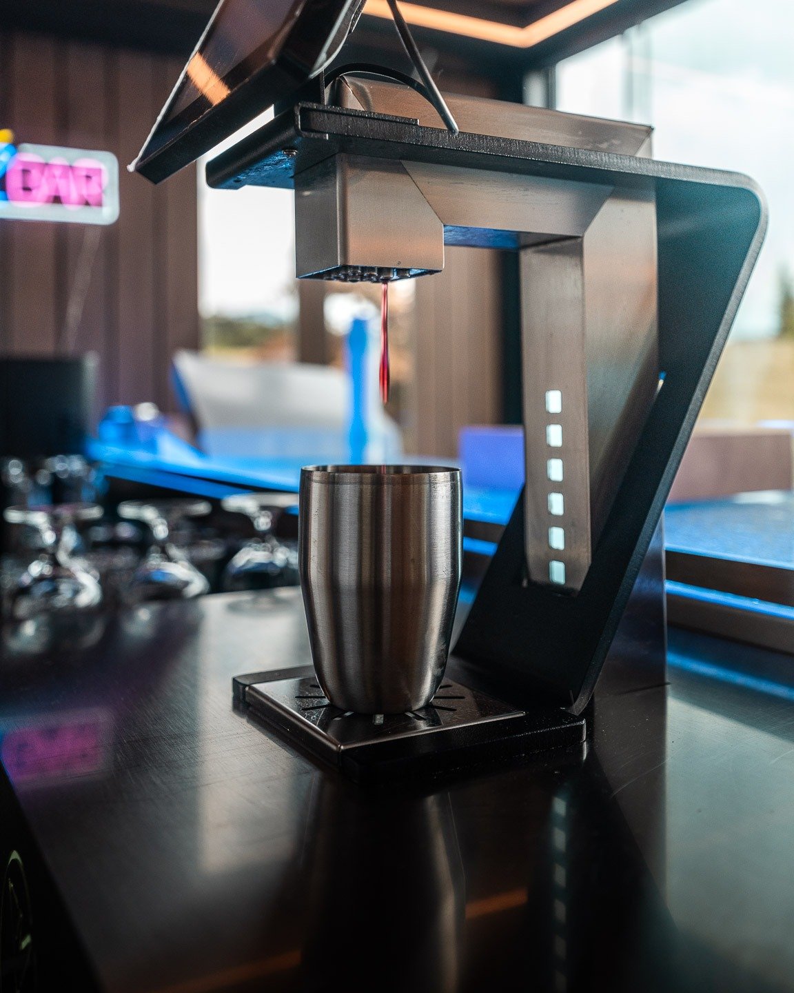 La machine à cocktails automatique de Secret Paradise servant une boisson dans un gobelet en inox, devant l'enseigne lumineuse du bar